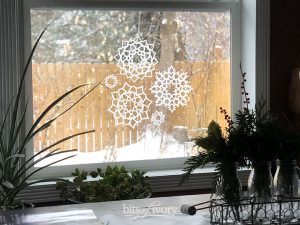 A winter view from a window with paper snowflakes on it.